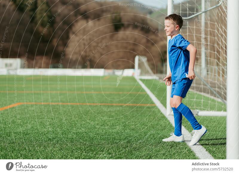 Young soccer player on the field ready for the game youth sport boy uniform blue goal green artificial turf stand focus football kid athlete outdoor competition
