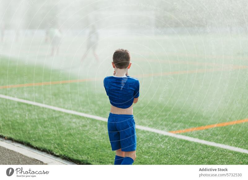 Young soccer player on misty field during sprinkler run boy sportswear football water background young child youth active outdoors recreation game grass green