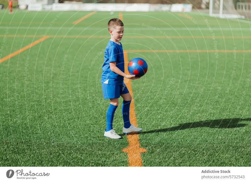 Young soccer player holding ball on field boy sport turf artificial green grass confidence uniform casual sportswear outdoor athletic child youth football game