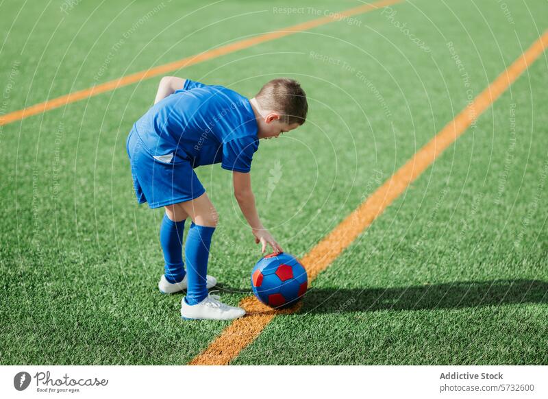 Young soccer player preparing for kickoff on field boy young athlete blue uniform bends ball red soccer ball white line green artificial turf game start sport