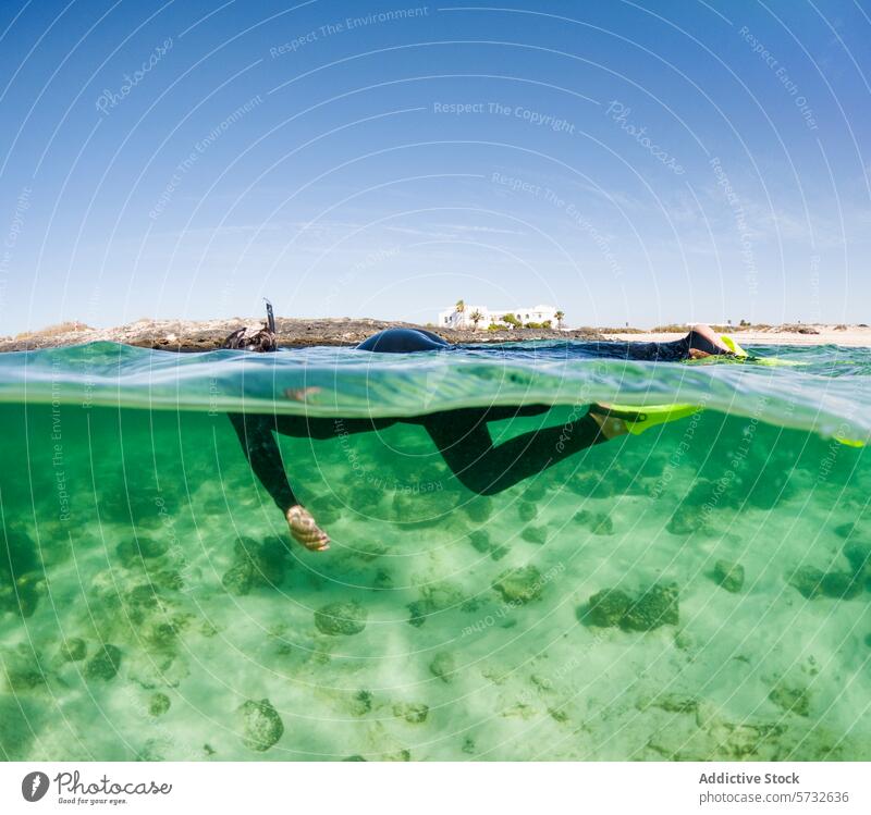Anonymous snorkeler, in focus, traverse the clear turquoise waters above a rocky seabed with a picturesque coastal background clear water snorkeling wetsuit fin