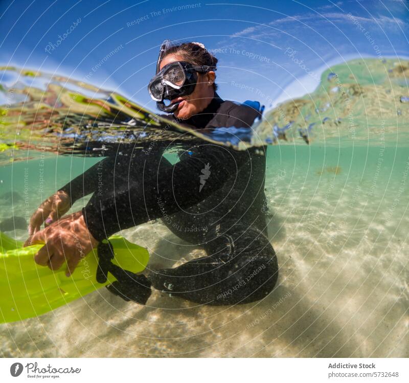 An adventurous snorkeler in a wetsuit is half-submerged in crystal clear waters, with sunlight dancing across the sandy bottom tropical adventure shallow mask