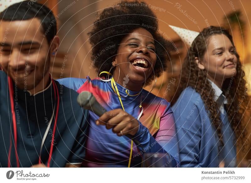 Portrait of Black young woman laughing with genuine emotion while enjoying party with friends at home group people Black woman karaoke diversity multiethnic