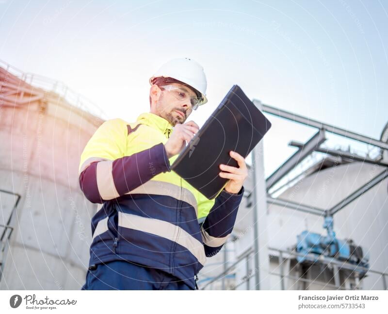 An engineer man making notes on his clipboard in a factory. Concept of Industry industry control supervisor uniform worker inspector architect hardhat audit