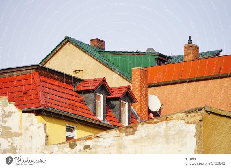 Residential buildings built close together with demolition walls, red and green tiled roofs, chimneys, satellite dishes, dormers, windows, roof terraces