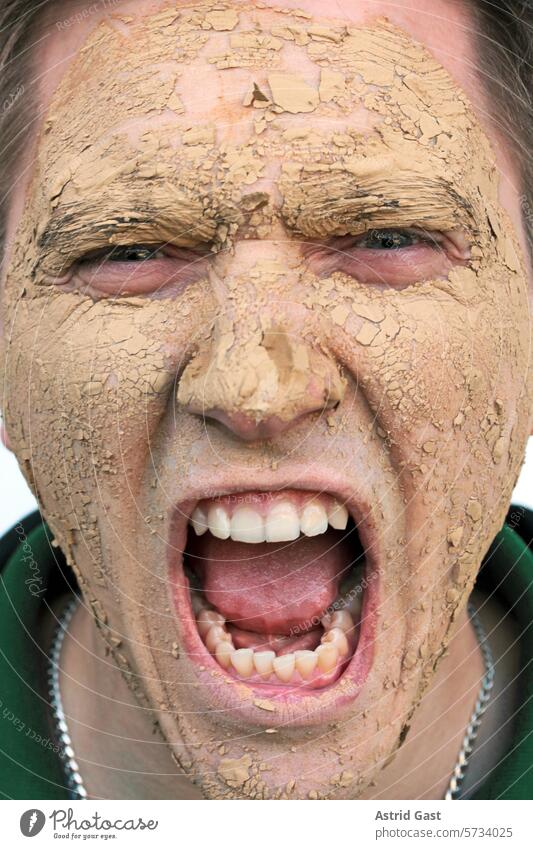 A screaming man with a mask made of earth Man Face Mask Scream shout healing earth Earth dirt frowzy filth Dirty Dry Skin Pain care beauty mask Shriveled cracks
