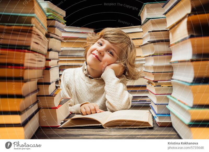 Dreamy little boy sitting at classroom or library desk. Smart child smiling, thinking about study or maybe school holidays, end of lesson book education