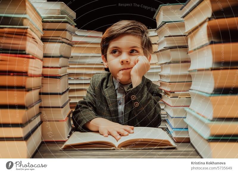 Cute little schoolboy reading interesting book in library between stacks of books literature. Education concept, time for kids pleasure. education study student