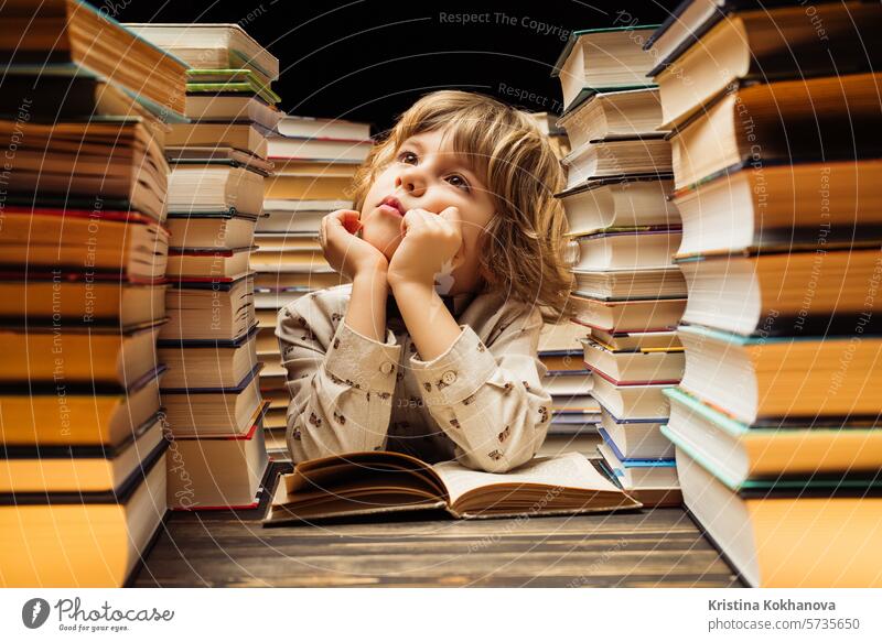 Dreamy little boy sitting at classroom or library desk. Smart child smiling, thinking about study or maybe school holidays, end of lesson book education