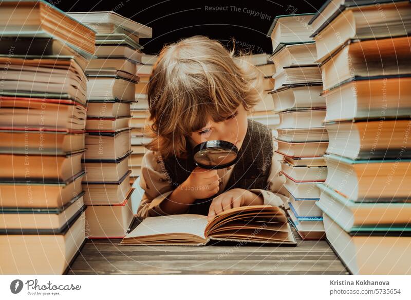 Little researcher boy reads book with magnifying glass in library. Cute clever preschooler playing, studying knowledge with instrument education literature