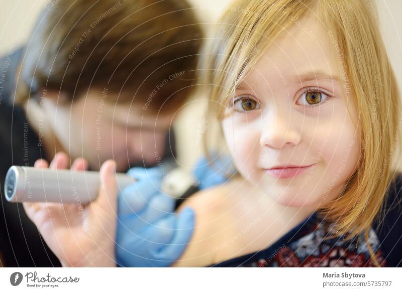 A caring doctor checks moles on the skin of a small child. A dermatologist looks at a rash on the back of a girl using a dermatoscope. appointment checkup kid