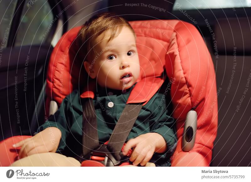 Cute toddler boy is in car seat. Portrait of pretty little child during family road trip. Kid scared by motion sickness or riding in vehicle at night time. Safety transportation of baby by car.