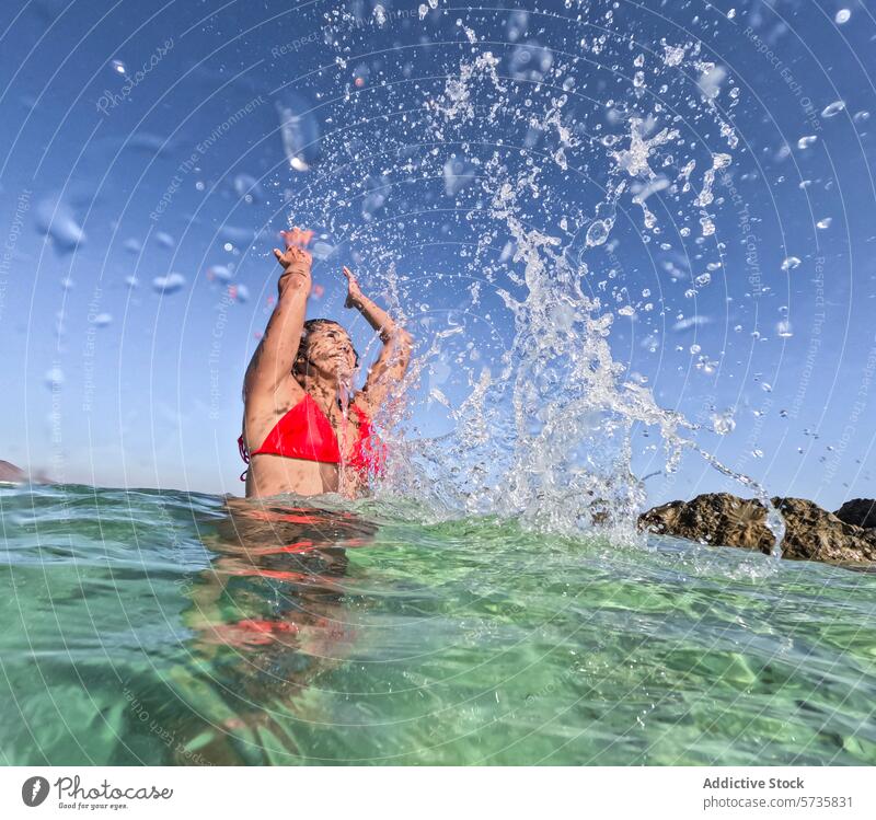 Joyful splash in crystal clear summer waters swim swimsuit red joy sea sunlight sparkle woman exuberant gleaming wave cool refreshing fun holiday vacation