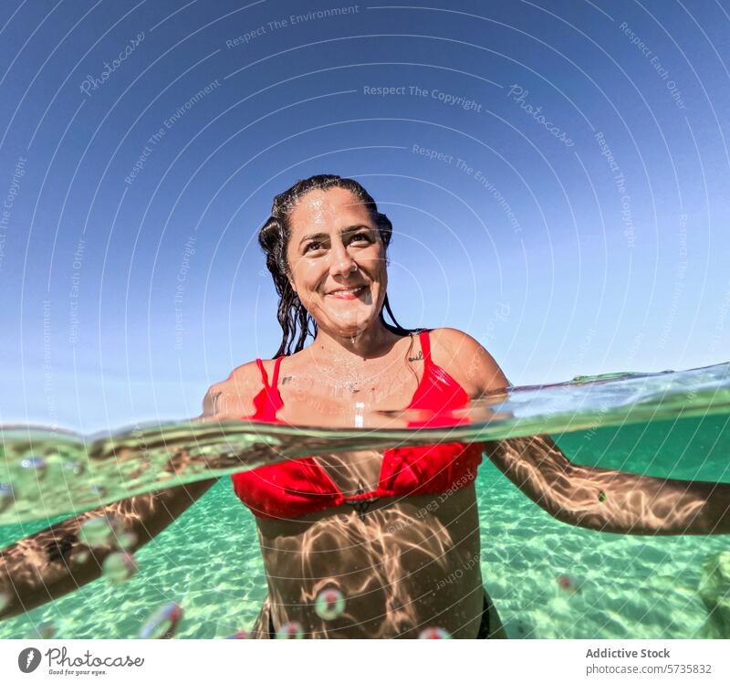 Woman Enjoying Summer Swim in Crystal Clear Water woman swim summer water clear tranquil smiling swimsuit red sunny day half-submerged sea ocean leisure