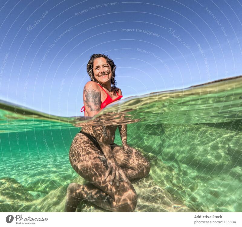 Serene Underwater Scene with Smiling Woman in Sunlight woman underwater sunlight patterns floating serene red swimsuit joy tranquil water surface smiling