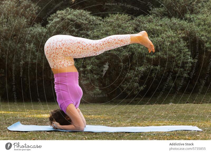 A dedicated yogi exhibits a perfect headstand pose on a yoga mat amidst the gentle backdrop of a sunlit park nature woman balance concentration fitness
