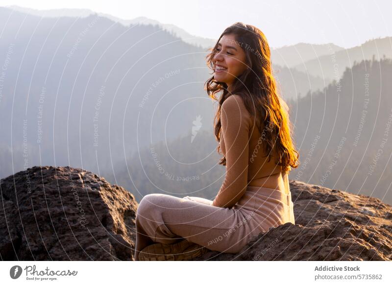 A joyful woman sits basking in the golden light of sunrise on a mountain peak, with a stunning backdrop of misty mountains serenity person female happy nature