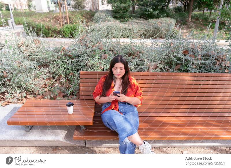 Urban woman relaxing with phone on park bench city smartphone coffee casual urban sitting outdoors engrossed using phone looking down technology leisure