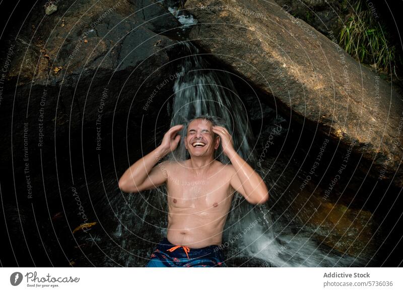 A man laughs with pure joy as he enjoys a natural waterfall shower in the heart of Langkawi's lush forest laughing Malaysia nature happiness outdoor rock stream