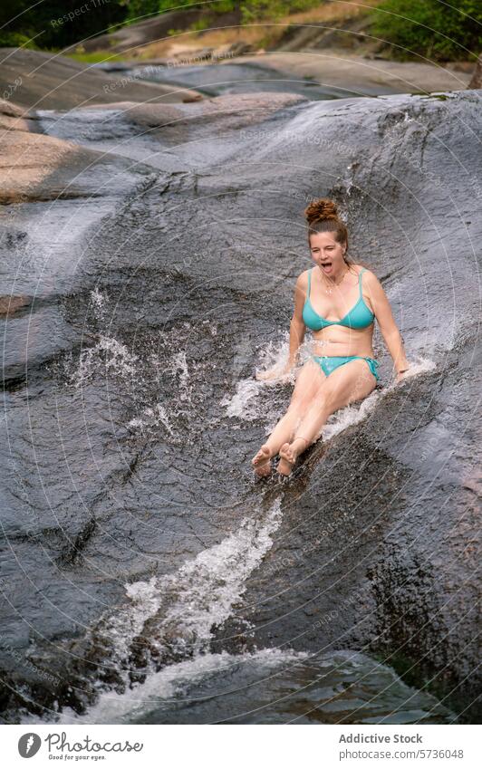 A woman glides with joy down a smooth, natural rock slide in the verdant forests of Langkawi, embracing the fun of nature river outdoor swimwear tropical