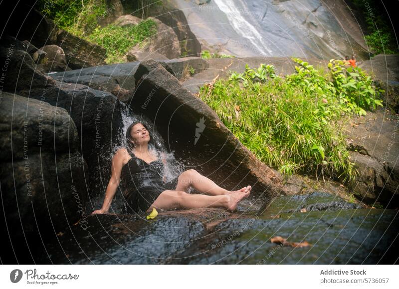 A woman reclines on a rock, feeling the gentle flow of a waterfall in the lush surroundings of Langkawi, Malaysia tranquil relax nature serene jungle natural