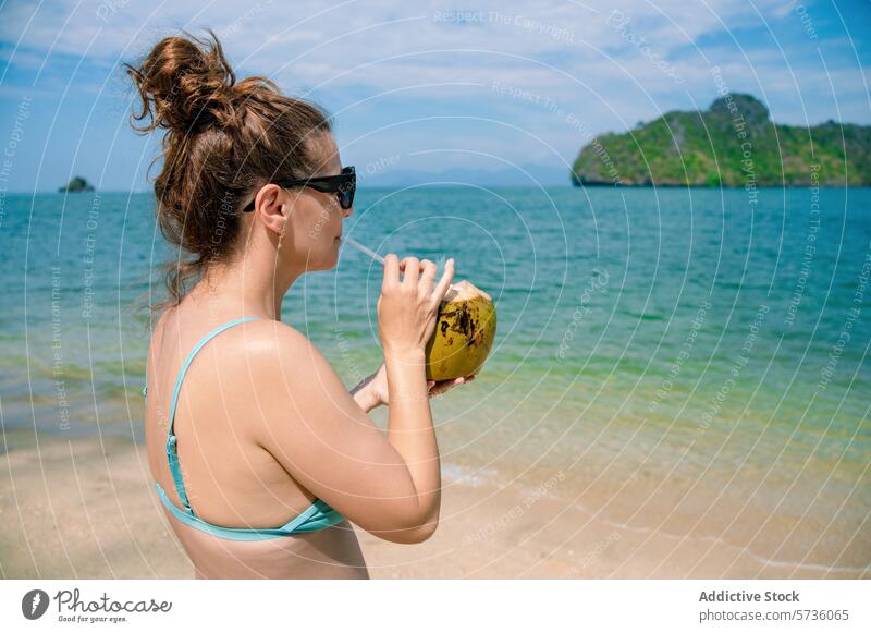 A woman savors a fresh coconut drink on a sunny beach with the picturesque Langkawi archipelago in the background refreshment tropical beverage summer leisure