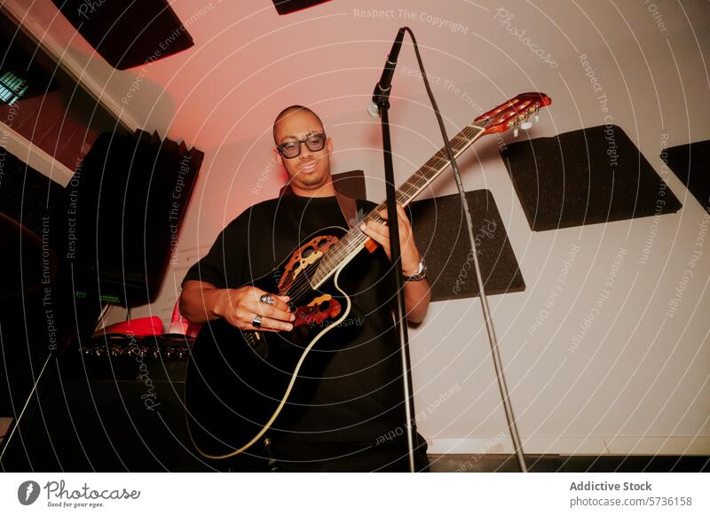 Male musician playing acoustic guitar in studio male microphone man band instrument glasses standing entertainment performer artist looking away soundproofing