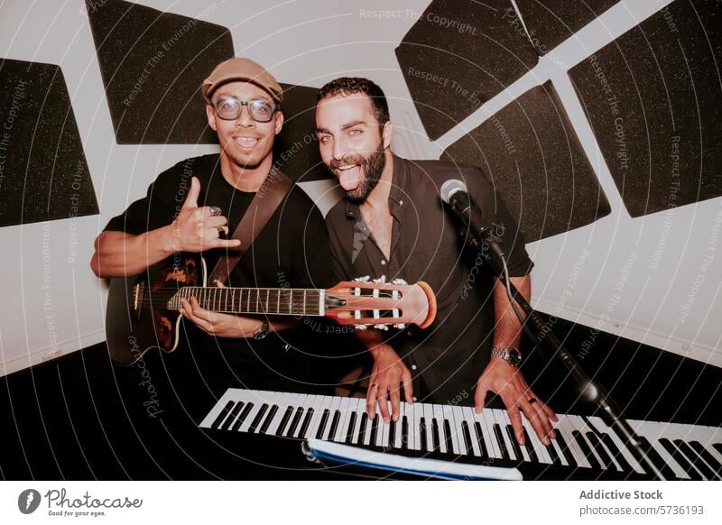 Two male musicians with guitar and keyboard in studio band electric guitar looking at camera performance playful enjoyment entertainment artist thumbs up duo