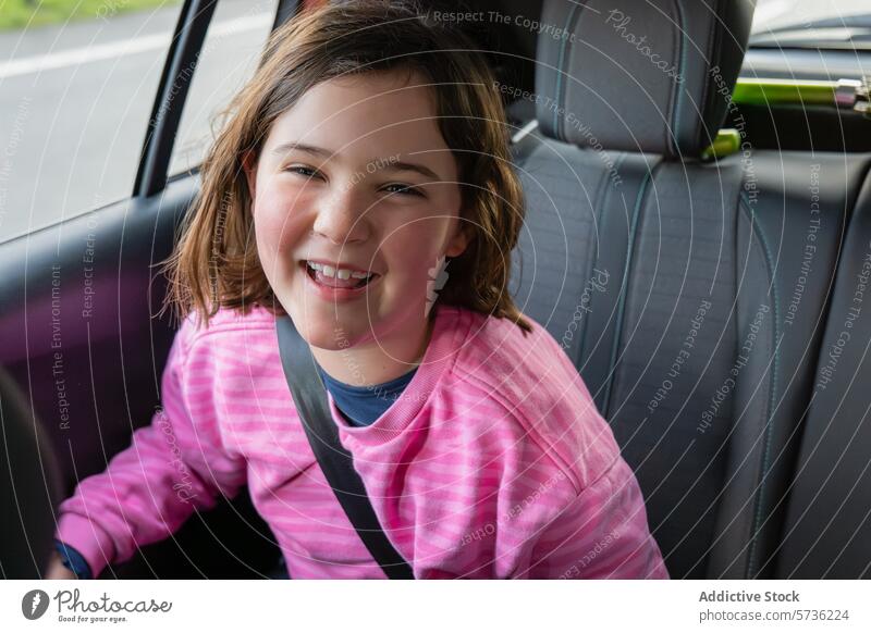 Joyful girl sitting in a car wearing a seatbelt child safety smile cheerful journey transport travel vehicle young happiness joy road trip secure protection
