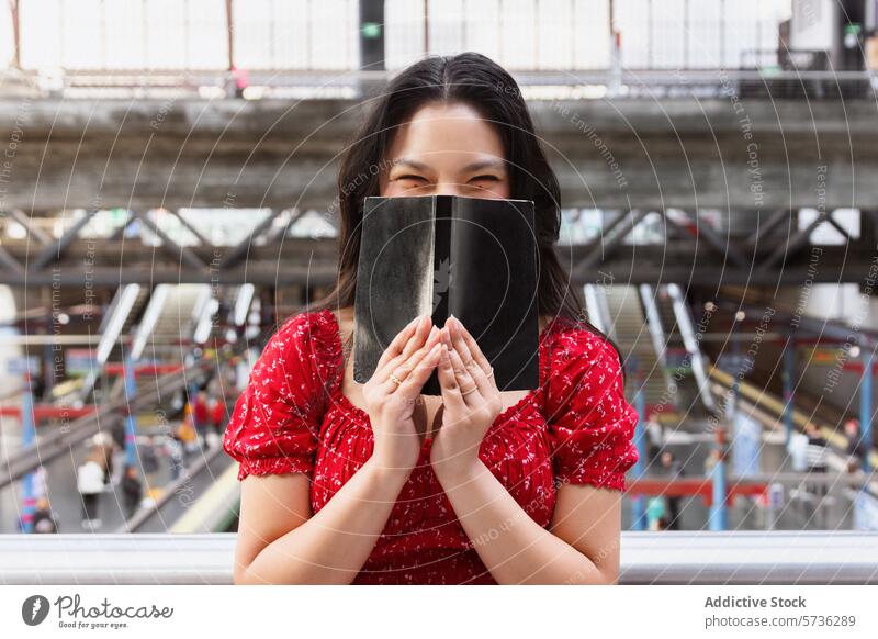 Woman in red dress covering face with book at station asian woman train station playful hide smile eyes cheerful platform commuter portrait busy travel public