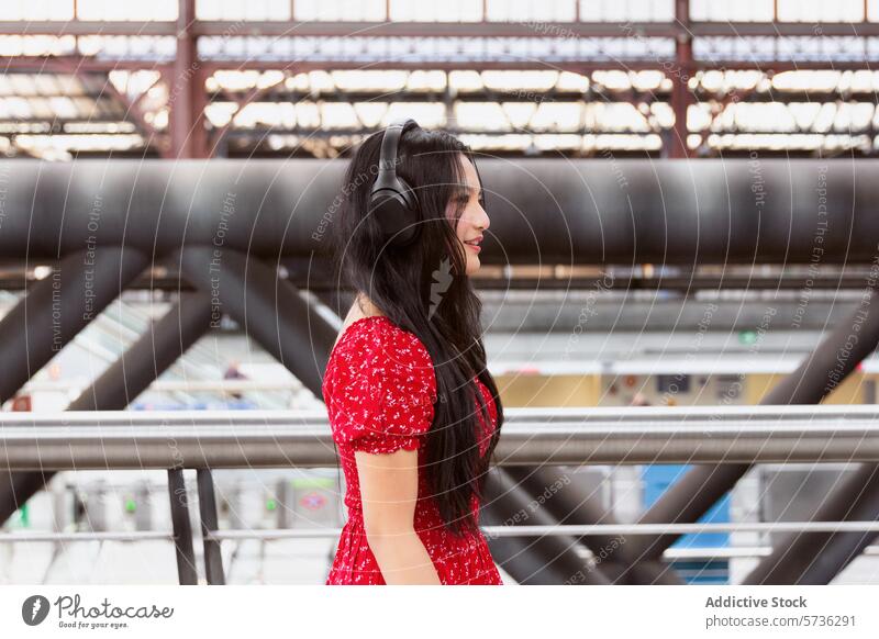 Woman in red with headphones at a train station asian woman dress music young adult female leisure technology transport railroad commute travel lifestyle casual