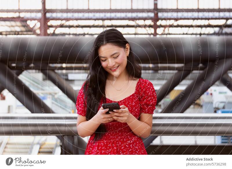 Young woman using smartphone at modern train station cheerful red dress young architecture city life background standing connectivity mobile technology travel