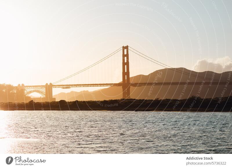The setting sun casts a golden silhouette of the Golden Gate Bridge, creating a serene scene over the bay with hazy mountain backdrops sunset San Francisco