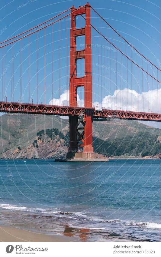 A stunning view of the Golden Gate Bridge as seen from the sandy shores, with gentle waves lapping at the beach and hills in the distance San Francisco