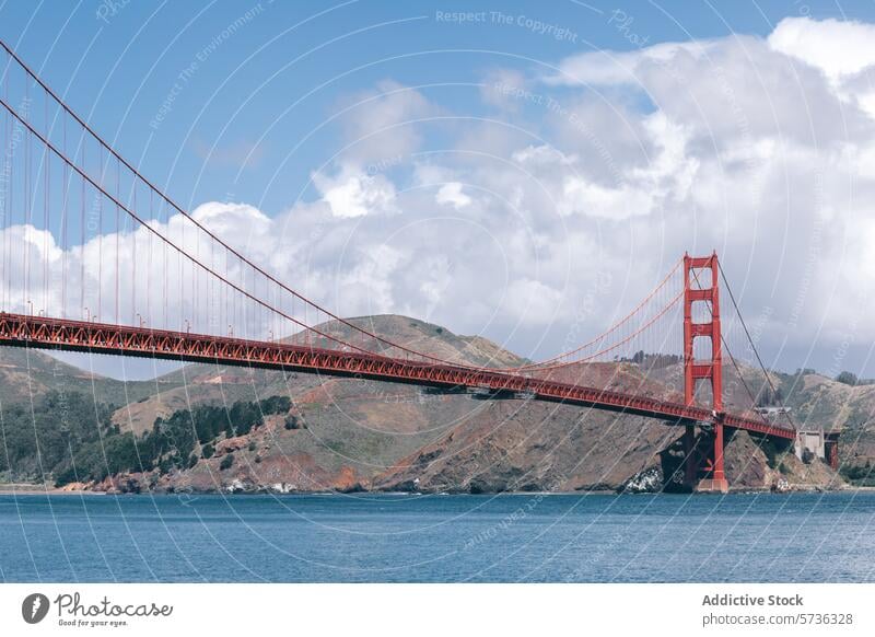 The Golden Gate Bridge stretches across blue waters against a backdrop of hills and fluffy clouds, showcasing San Francisco's iconic landmark suspension bridge