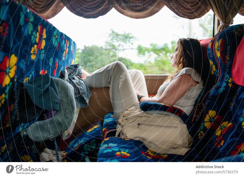 Woman relaxing on a colorful bus seat during travel woman window gaze resting floral pattern backpack travel pillow commuter transportation journey adventure