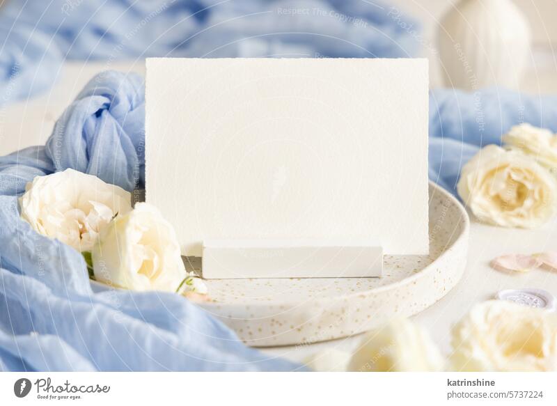 Card near light blue tulle fabric and cream flowers on plate close up, copy space, wedding mockup card romantic knot white silk roses spring mothers day ivory