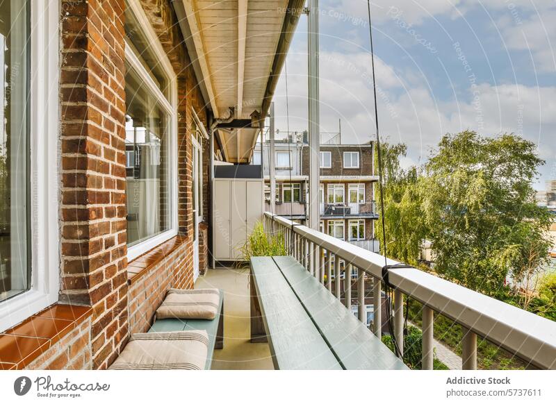 Cozy balcony with a view of the neighborhood furniture seat wooden rail residential area brick window exterior building apartment urban greenery peaceful