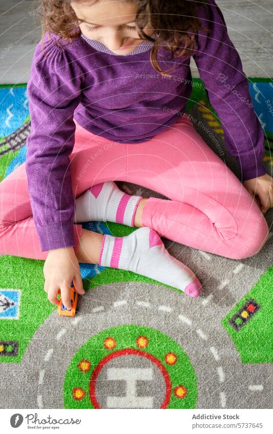 Child playing with toy car on a colorful playmat child girl creativity enjoyment indoor overhead view vibrant playtime young female sitting floor carpet game