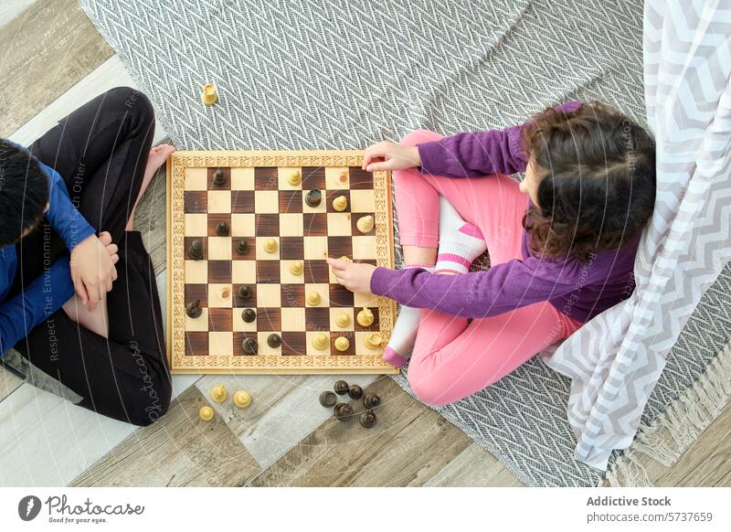 Two kids engaged in a game of chess at home child play board wooden strategy cognitive skill indoor rug boy girl overhead view comfort sitting leisure activity