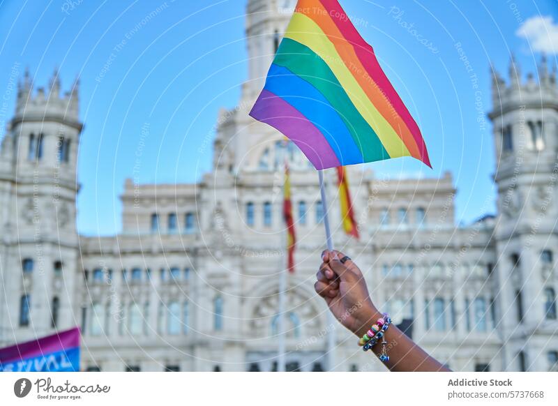 Hand waving rainbow flag at LGBTIQ pride event lgbtiq hand arm solidarity historical building backdrop celebration diversity inclusion identity gay lesbian