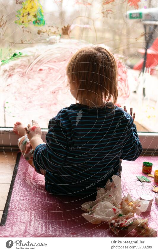 A child draws on a window with his feet children's art Life with children Red Yellow variegated Hand Fingers Joy fun Window painting Creative with children