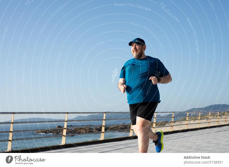Overweight man jogging by the sea on a clear day overweight fitness health running exercise seaside promenade adult male blue sky outdoor sportswear active