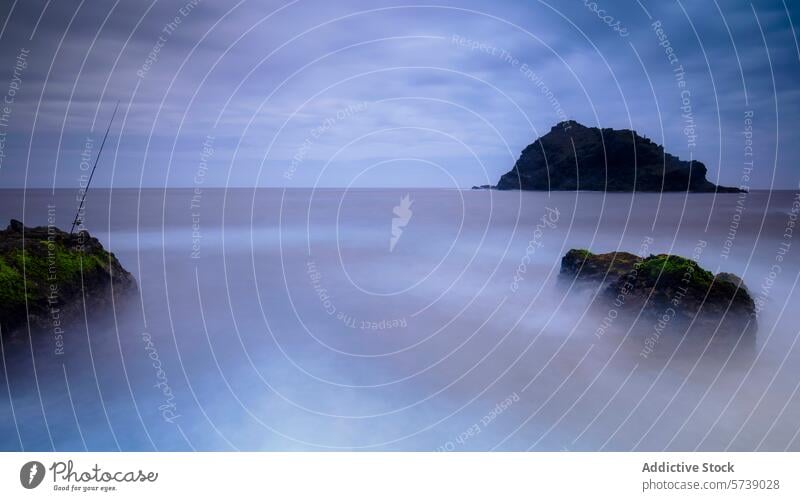 A lone fishing rod stands on the rocky shore of Garachico, with a mystical islet shrouded in a sea mist at dawn morning nature landscape ocean serene tranquil