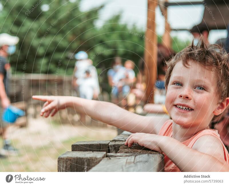 With sparkling eyes and a joyful smile, a young boy points excitedly at something off-camera at a bustling summer farm school pointing attraction child
