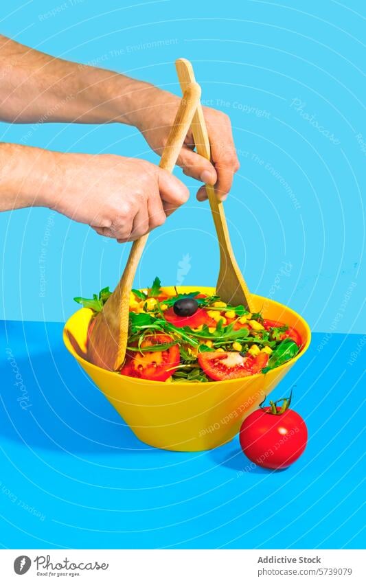 Fresh salad preparation with wooden utensils fresh hands yellow bowl blue background food healthy nutrition tomato arugula olive corn meal diet lunch mix