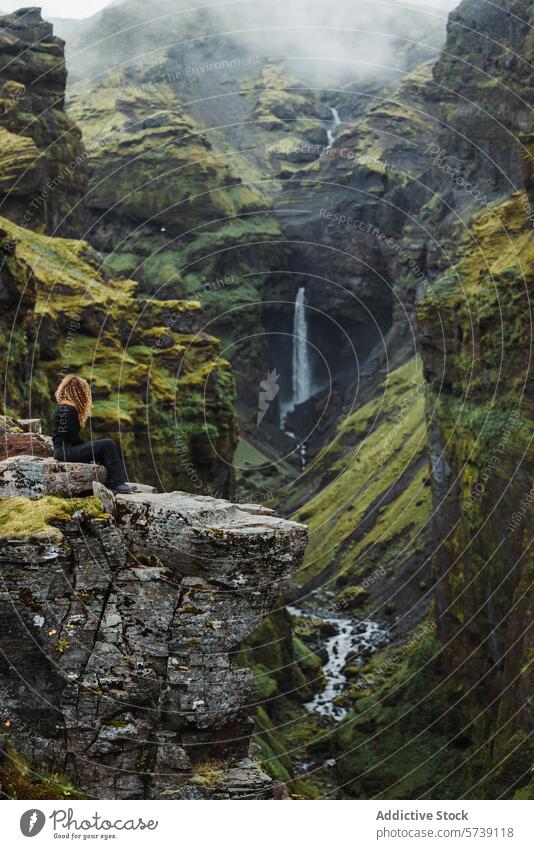 Anonymous woman sitting on cliff contemplating Nature at a Secluded Icelandic Waterfall iceland waterfall nature adventure solitude greenery landscape traveler