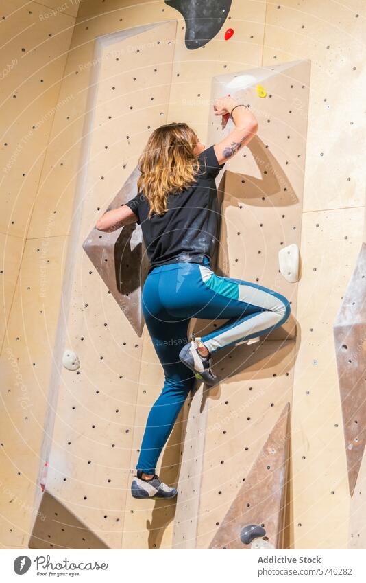 Athletic woman scaling an indoor climbing wall athletic sportswear grip strength challenge active fitness exercise activity leisure hobby workout muscle
