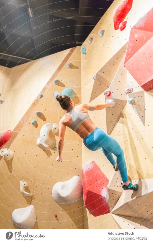 Climber ascending on an indoor bouldering wall climber female strength agility skillful challenge colorful holds sport fitness exercise training grip