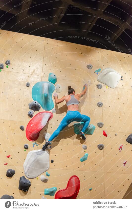 Athletic woman scaling an indoor climbing wall athletic sport hold stretch reach colorful exercise activewear fitness gym bouldering challenge skill hobby